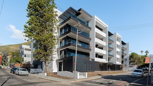 Um edifício moderno de vários andares com varandas, área de estacionamento e vista para a rua.