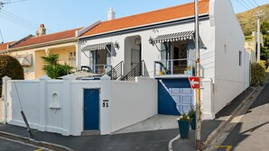 A white building with a red-tiled roof, a blue garage door, and a staircase leading to the entrance. - Grecian Haven In Greenpoint Pool and Braai (Cape Town)