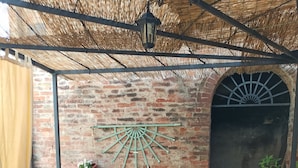 Un espacio al aire libre techado con mobiliario de madera y un muro de ladrillo de fondo.