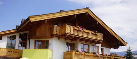 A chalet-style building with wooden balconies, large windows, and a mountain backdrop.