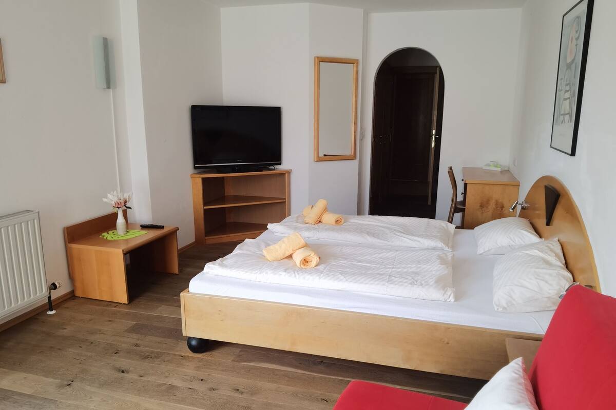 Ein Hotelzimmer mit einem hölzernen Bett, einem roten Sofa, einem Fernseher auf einem Schrank und einem Holztisch.