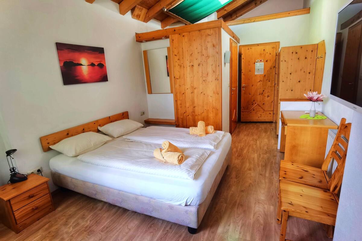Ein Schlafzimmer mit einem hölzernen Bett, einem Nachttisch, einem Schreibtisch mit Stuhl und einem Spiegel.