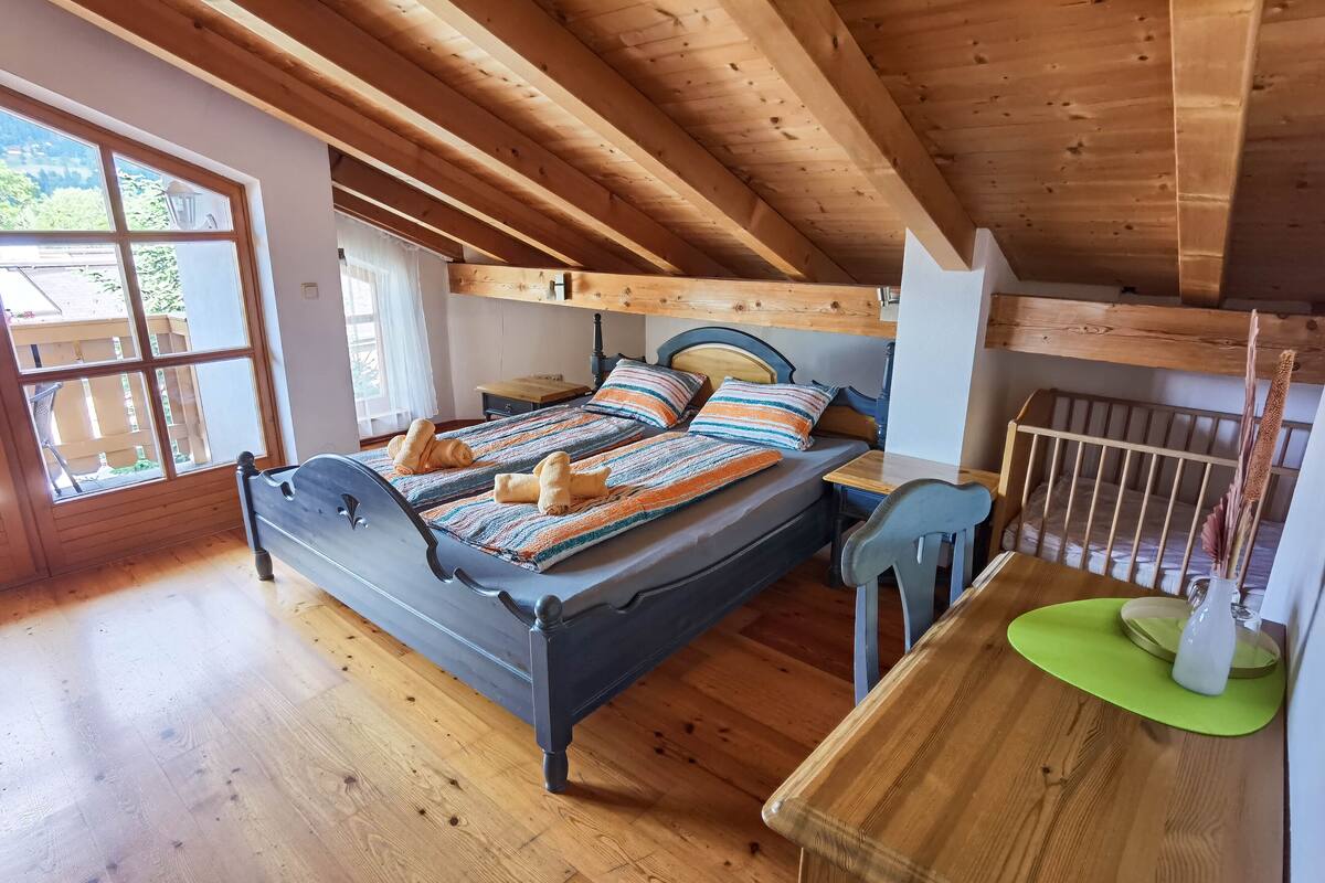 Ein Schlafzimmer im Dachgeschoss mit Holzbalken, einem Bett, einem kleinen Tisch und einem Fenster.