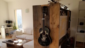 Uma sala de estar com divisória de madeira, um violão, um sofá, uma mesa de centro com xadrez e uma estante de livros.