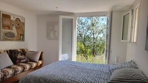 Quarto com uma cama, um sofá e uma porta que dá para uma varanda com árvores.