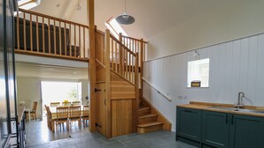 A spacious kitchen with dark grey tiles, a wooden staircase, and a dining area with a table and chairs. - Pen y Mynydd (Newport)