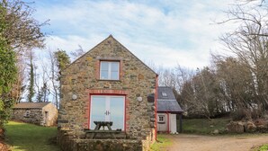 A stone cottage with a red door and a small table outside. - Pen y Mynydd (Newport)