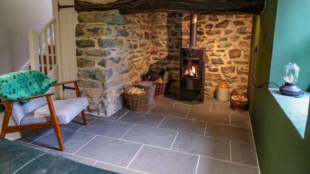 A stone-walled room with a fireplace, a chair, and a table with a lamp. - Pen y Mynydd (Newport)