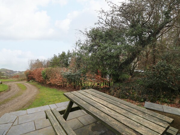 A wooden picnic table in a park with a dirt path and trees in the background.