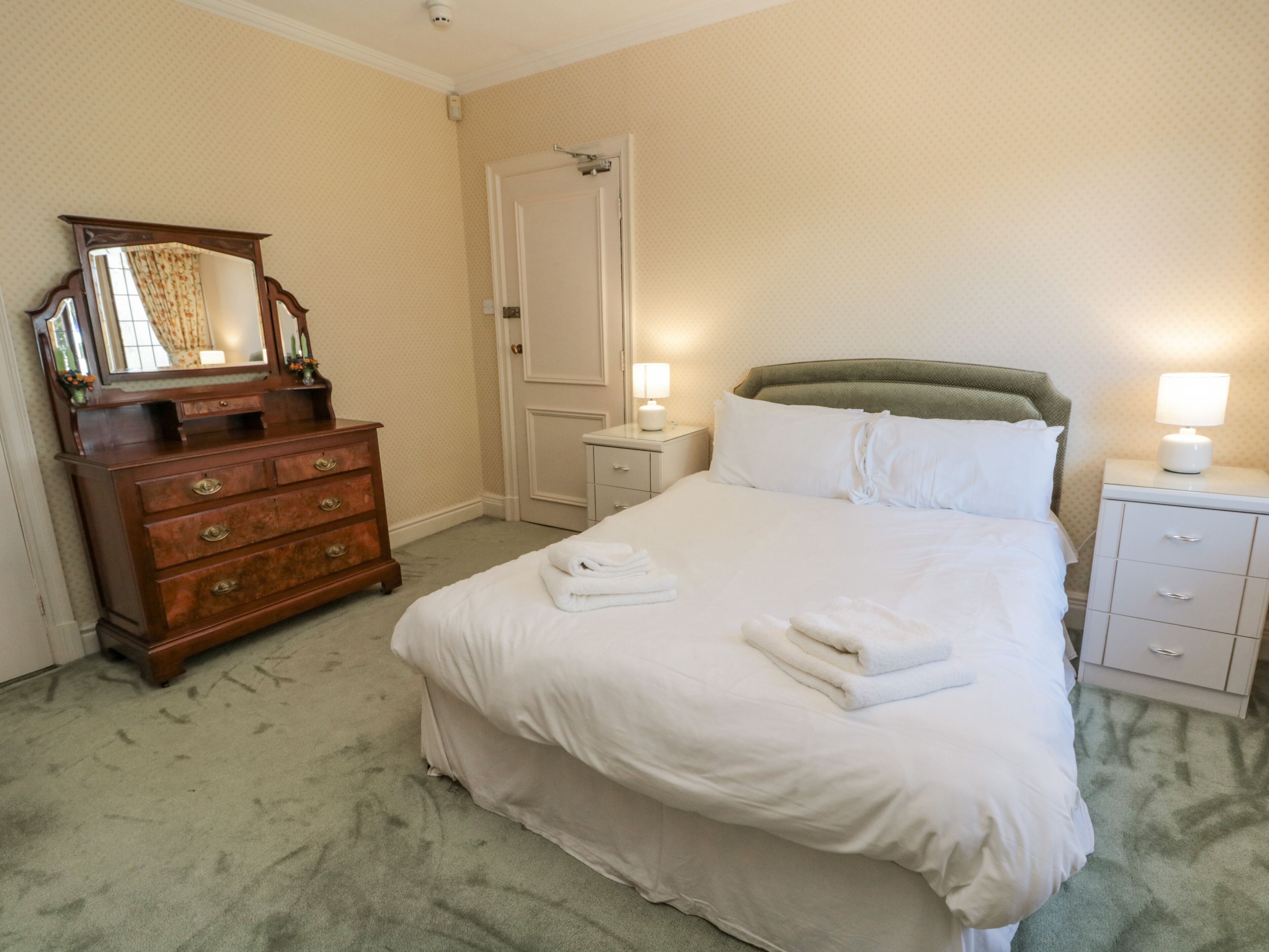 A neatly arranged hotel room with a large bed, a dresser, a mirror, and two bedside lamps.