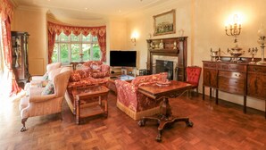 A traditional living room with a fireplace, wooden furniture, and a large window. - Highcliffe Manor (Bridlington)
