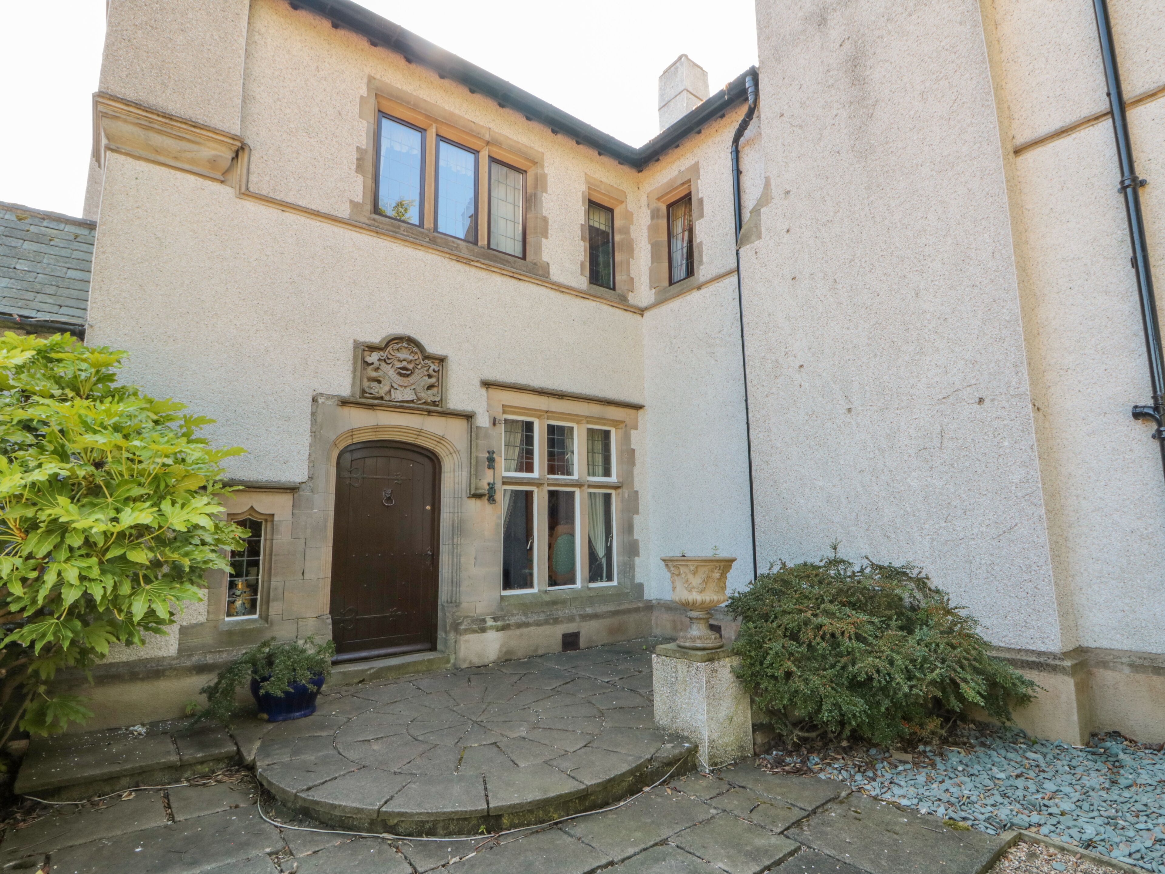 A building with a stone facade, a central entrance with a brown door, and a small garden area with potted plants and a stone pathway.