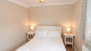 A hotel room with a large bed, two bedside tables with lamps, a ceiling light, and a radiator. - Highcliffe Cottage (Bridlington)