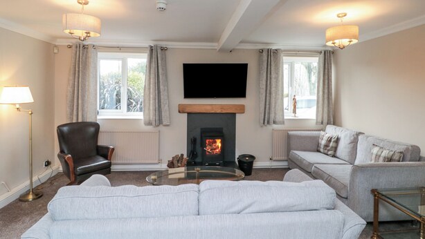 A living room with a fireplace, two sofas, a chair, and a TV mounted on the wall. - Highcliffe Cottage (Bridlington)