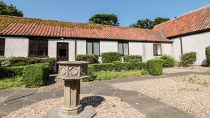 A building with a tiled roof, a stone pedestal with carvings, and a gravel pathway. - Highcliffe Cottage (Bridlington)