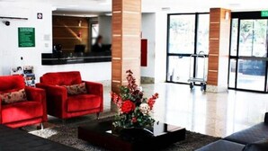 A modern lobby with red sofas, a black coffee table with flowers, and a reception desk. - Sun Square Suítes Hotel By Lual (Goiânia)