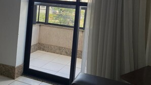 A room with a large sliding glass door leading to a balcony. The balcony has a tiled floor and a view of tall buildings and greenery. - Sun Square Suítes Hotel By Lual (Goiânia)