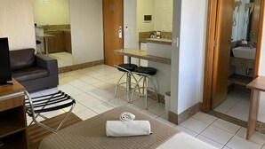 A hotel room with a sofa, a small table, a bar stool, a TV, and a bathroom visible through an open door. - Sun Square Suítes Hotel By Lual (Goiânia)