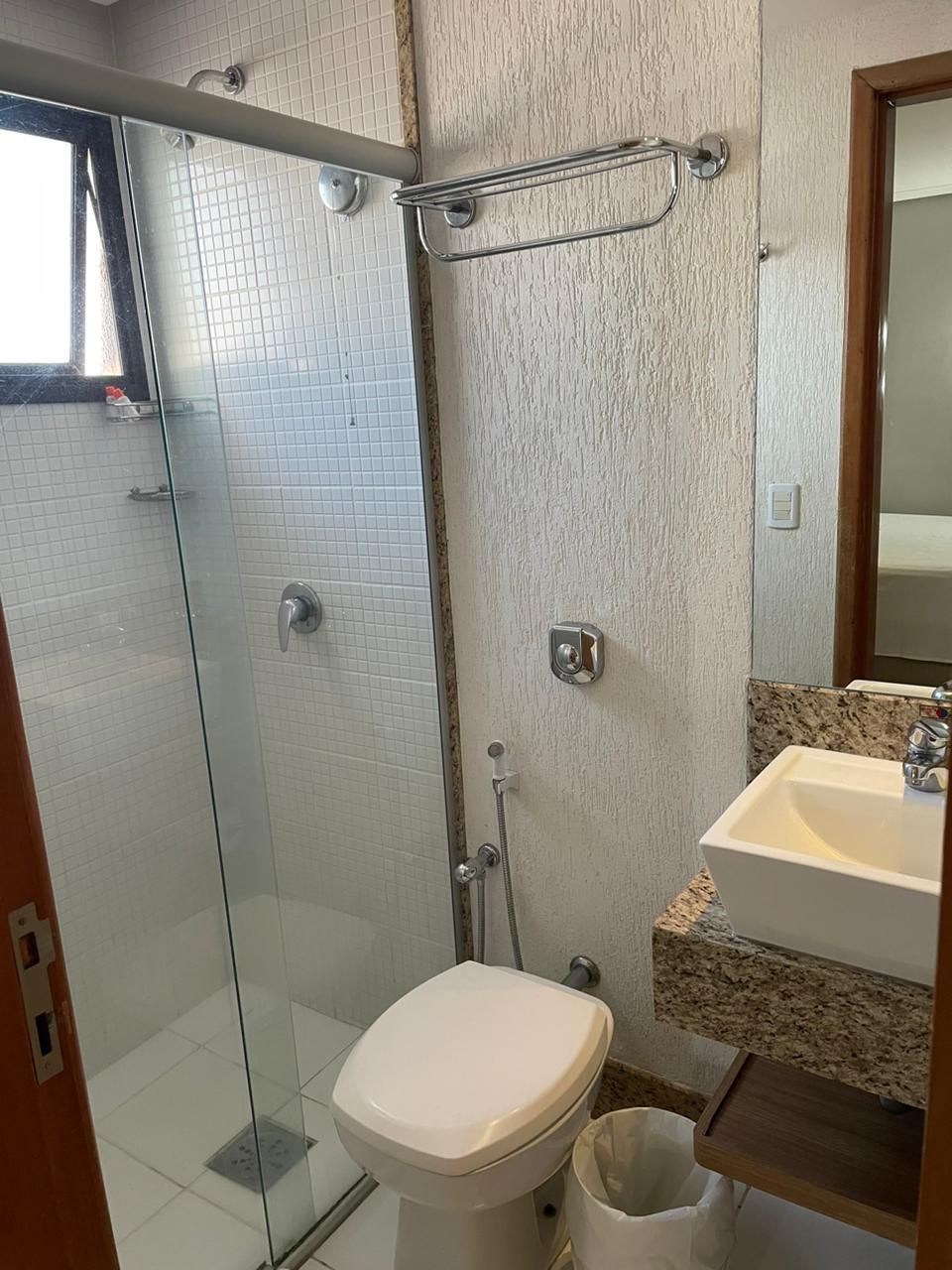 Un baño con cabina de ducha de vidrio, inodoro blanco, lavamanos con encimera de granito y espejo sobre el lavamanos.