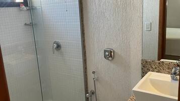 Un baño con cabina de ducha de vidrio, inodoro blanco, lavamanos con encimera de granito y espejo sobre el lavamanos.