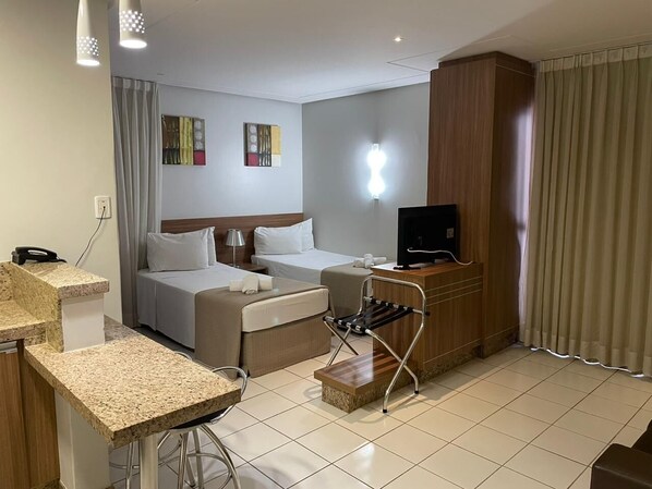 Habitación de hotel con cama, escritorio, silla, televisión y una kitchenette pequeña.