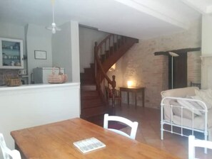 Ein Essbereich mit Holztisch und -stühlen, eine Treppe, die zu einer oberen Etage führt, und eine gemütliche Sitzecke mit einem weißen Sofa.