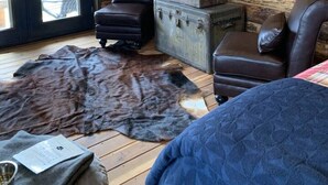 Une pièce rustique aux murs en bois, avec un fauteuil en cuir, une petite commode et un tapis en fourrure.