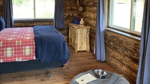 Une chambre rustique dans un chalet, comprenant un lit, une petite table, un panier pour animaux de compagnie et un ventilateur de plafond.