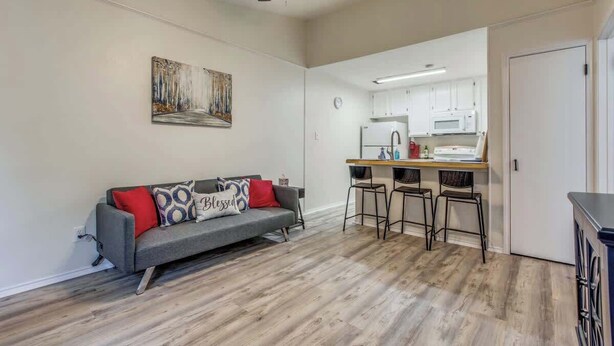 A living room with a gray sofa, red and patterned pillows, a ceiling fan, and a kitchen area with white cabinets and a microwave. - Cozy Medical Center Retreat in San Antonio (San Antonio)