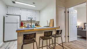 A compact kitchen with white cabinets, a microwave, a refrigerator, a wooden countertop, and two bar stools. - Cozy Medical Center Retreat in San Antonio (San Antonio)