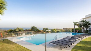 Una piscina con sillones de descanso, un socorrista y vistas al océano.