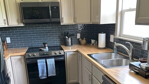 Una cocina moderna con armarios blancos, un salpicadero de azulejos negros, electrodomésticos de acero inoxidable y encimera de madera.
