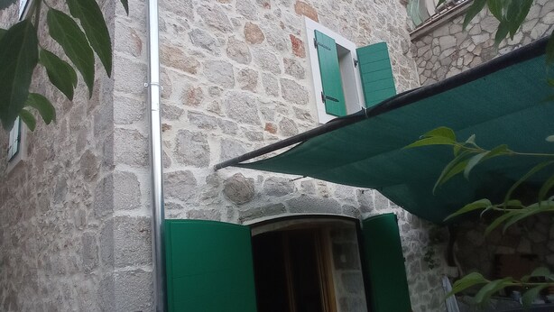Un bâtiment en pierre avec une porte en bois et des volets verts.