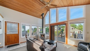 A spacious living room with a large leather sofa, a fireplace, and a view of the neighborhood through large windows. - Stargazer-1/2 blk to the beach and golf course, ocean view from deck MCA#251 (Manzanita)