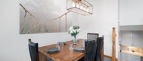 A dining area with a wooden table set for six, surrounded by chairs. A modern pendant light hangs above the table.