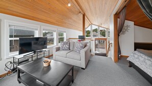 A modern living room with a wooden ceiling, a grey sofa, a flat-screen TV, and a dining area with a table and chairs. - Stargazer-1/2 blk to the beach and golf course, ocean view from deck MCA#251 (Manzanita)