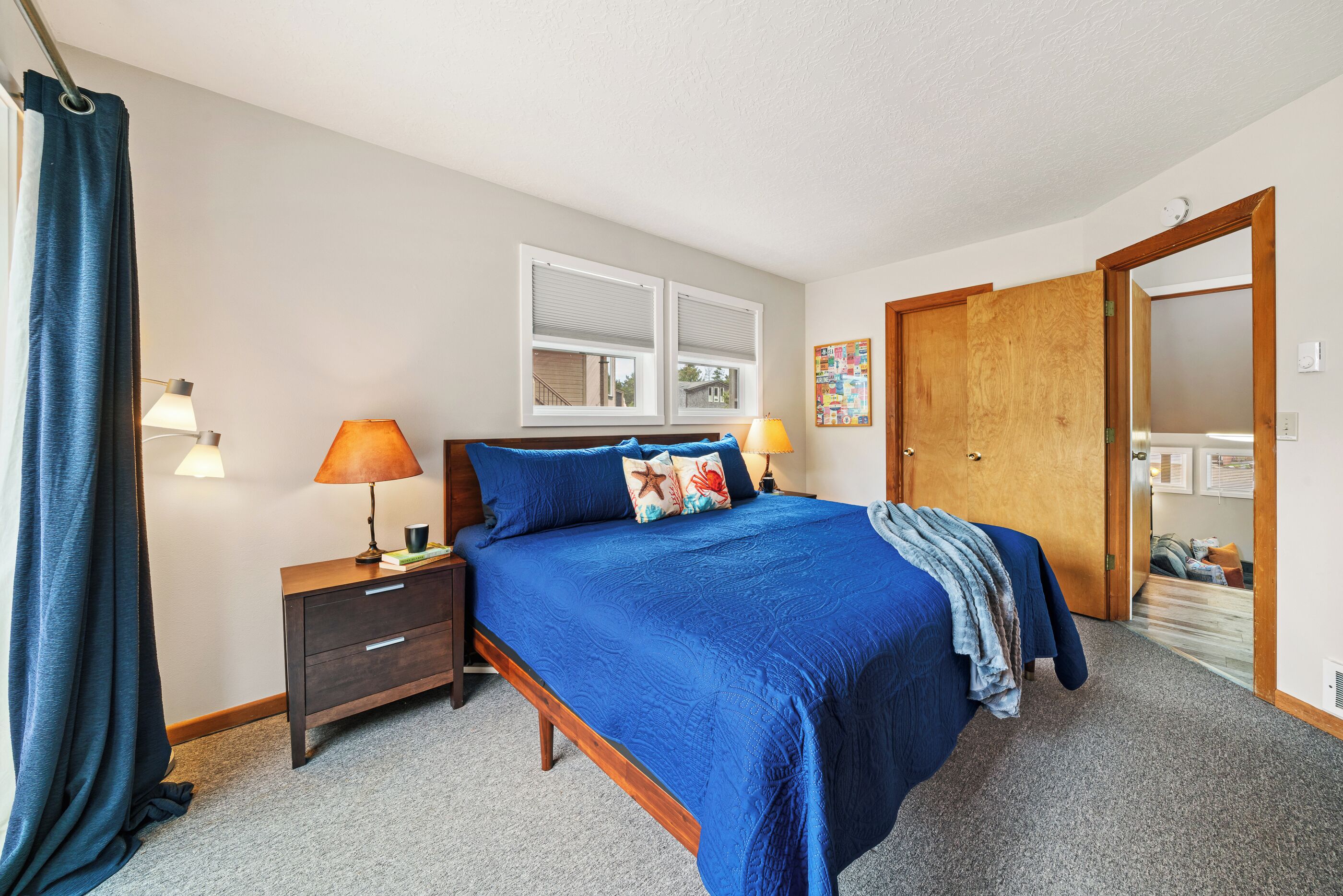 A bedroom with a large bed, a wooden nightstand, a desk, and a door leading to another room.
