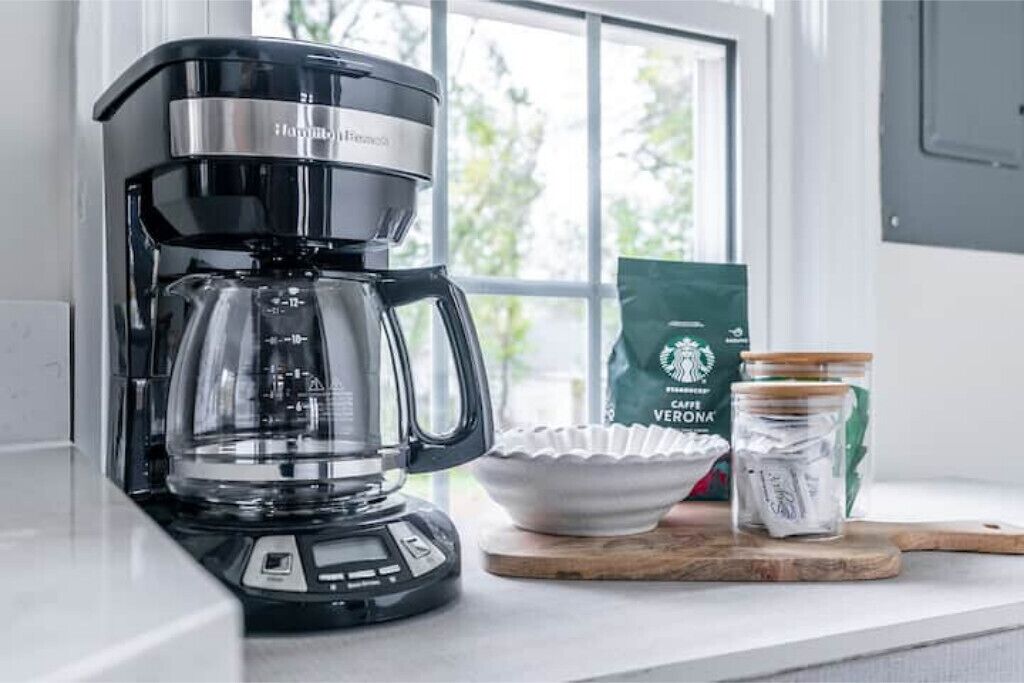A black coffee maker on a kitchen counter with a window in the background.