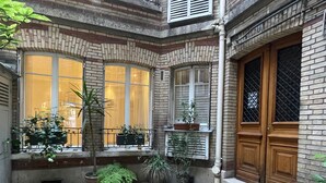 A courtyard with a tiled floor, potted plants, and a wooden door. - Village des Batignolles Paris 17 (Paris)