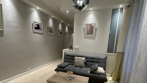 A modern living room with a grey sofa, a wooden coffee table, and a ceiling light fixture. - Village des Batignolles Paris 17 (Paris)