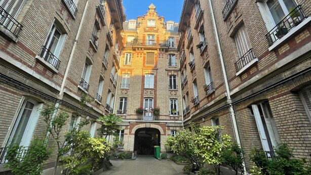 A courtyard with a central archway surrounded by brick buildings with balconies and windows. - Village des Batignolles Paris 17 (Paris)