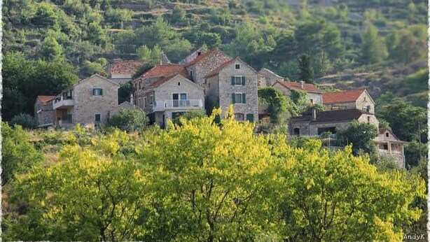 Un ensemble de bâtiments en pierre, à plusieurs étages et dotés de balcons, entouré d’une végétation luxuriante et de vignobles.