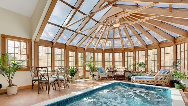 A sunlit conservatory with a pool, wooden beams, and potted plants.