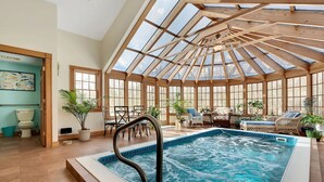 An indoor swimming pool with a glass ceiling, surrounded by seating and potted plants.