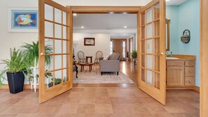 A spacious living area with a large open door leading to a dining area, a sofa, and a kitchen with wooden cabinets.