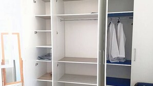 A walk-in closet with multiple shelves and hanging space, a mirror, and a blue bed. - Au Cœur de Sidi bou Said s+1 (Site archéologique de Carthage)