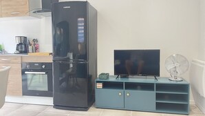 Een moderne keuken met een zwarte koelkast, een televisie op een blauwgroene standaard en een kleine ventilator.