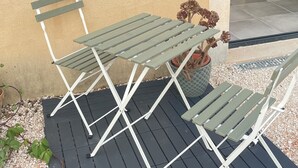 Een terras met een tafel, stoelen, een bloempot en een blik op een aangrenzende kamer.