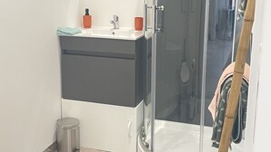 Een moderne badkamer met een douchecabine van glas, een witte wastafel met een donkere kast, en een toilet.