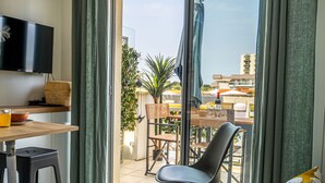 Un salon moderne doté d’un téléviseur, d’un coin repas avec des chaises et une table, et offrant une vue sur la ville grâce à de grandes fenêtres.